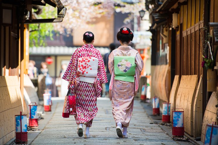 A geisha and a helper walk through Gion, Kyōto, side by side.